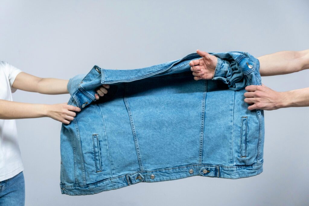 Two individuals pulling on a blue denim jacket, highlighting fashion and tension.